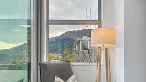 A room with a view of mountains, a chair with cushions, and a floor lamp. - Iconic Lake View Apt | Ski Lockers (Queenstown)