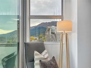 A room with a view of mountains, a chair with cushions, and a floor lamp.