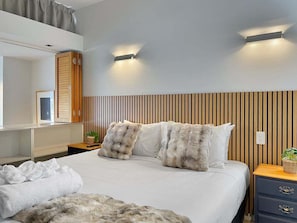 A modern hotel room with a large bed, two bedside tables, a wooden headboard, and wall-mounted lighting.