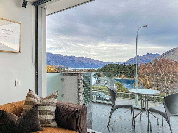 A balcony with a view of mountains and a lake, a round table, and two chairs.