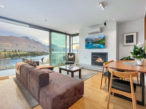 A modern living room with a large window, a sofa, a fireplace, and a dining area.