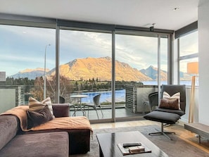 A modern living room with a large sliding glass door leading to a balcony with a view of mountains and a lake.