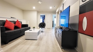 Ein modernes Wohnzimmer mit einem schwarzen Ledersofa, roten Kissen, einem weißen Hocker, einem schwarzen Sessel, einem Flachbildfernseher und einer Küchenzeile mit einem schwarzen Schrank und einer roten Akzentwand.