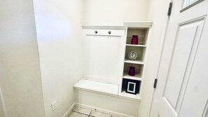 Een kleine, witte badkamer met een toilet, een plank met een klok en een rode vaas.