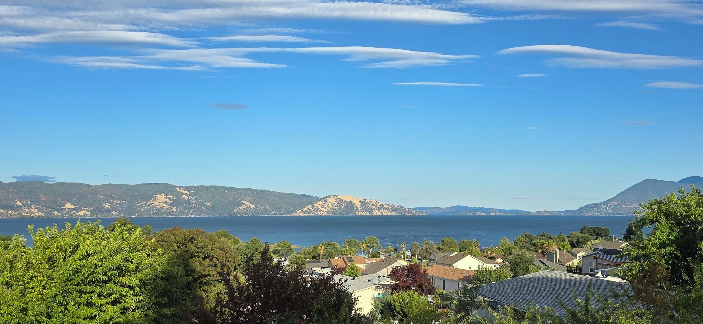 Un área residencial costera con casas, cielo despejado y montañas al fondo.
