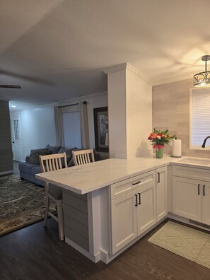 A kitchen with white cabinetry, a marble countertop, and a dining area with a wooden table and chairs. - Panoramic Water Views - Pet Friendly &  Fisherman's Specials (Lakeport)