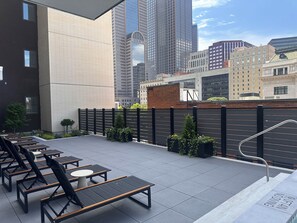 Eine Dachterrasse mit Außenbestuhlung, einem schwarzen Zaun und Stadtgebäuden im Hintergrund.