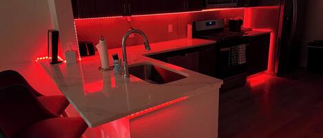 Una cocina moderna con una isla central, electrodomésticos de acero inoxidable e iluminación roja debajo de los armarios.