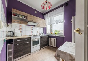 Een keuken met een witte kookplaat, donker houten kastjes, een witte koelkast en een raam met kantgordijnen.