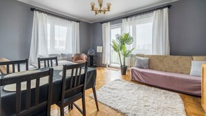 Ruokailutila, jossa on pöytä ja tuoleja, sohva, kattokruunu ja ruukkukasvi.