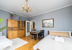 Una habitación con cama, una mesa de comedor, armarios de madera, una araña y un cuadro en la pared.