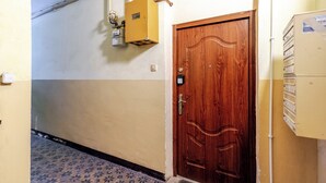 Un pasillo con una puerta de madera, un cuadro eléctrico y un termostato en la pared.