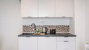 Una cocina con armarios blancos, encimera negra, salpicadero de azulejos hexagonales, un hervidor, un tostador y un lavabo con grifo.