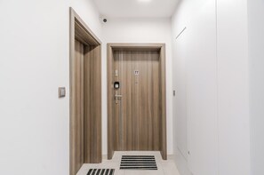 Ein Flur mit zwei Holztüren, davon eine mit der Nummer 77, und einem Lüftungsgitter an der Decke.