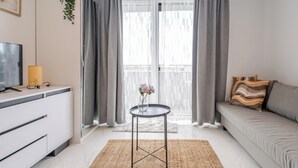 Una sala de estar moderna con un sofá, un televisor, una mesita con un florero y cortinas grises.