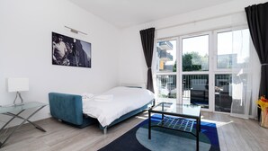 Quarto de hotel moderno com cama, mesa de vidro, sofá azul, uma janela grande com vista e um quadro na parede.