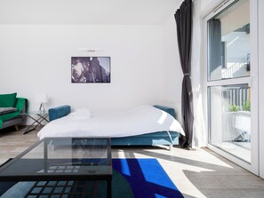Een moderne hotelkamer met een bed, een glazen salontafel, een groene fauteuil, een blauwe bank en uitzicht op de stad.