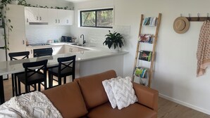 A modern kitchen with white cabinets, a central island, and a dining area with a brown sofa and chairs.