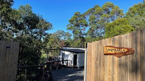 A wooden gate with a sign reading 'SHAMBARLA,' a small building, and a fenced area with trees in the background.