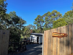 A wooden gate with a sign reading 'SHAMBARLA,' a small building, and a fenced area with trees in the background.