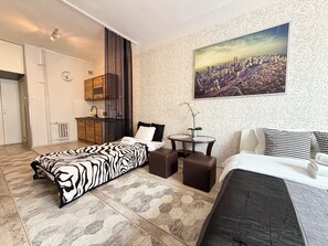 A modern bedroom with a cityscape view, a bed, a sofa, a small table, and a kitchen area. - Wrocław Rynek Downtown Studio (Wrocław)