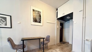 Una stanza con un tavolo di legno, due sedie, un tappeto decorato, una mappa incorniciata appesa al muro e un mobiletto bianco.