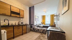 Una camera d'albergo compatta con angolo cottura, un letto con coperta a motivi zebrati, un piccolo tavolo da pranzo e una sedia.