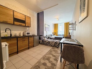 A compact hotel room with a kitchenette, a bed with a zebra-patterned blanket, a small dining table, and a chair. - Wrocław Rynek Downtown Studio (Wrocław)