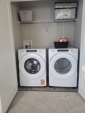 Une buanderie équipée de deux lave-linge Whirlpool, d’une étagère contenant des articles de rangement et d’une petite boîte blanche.