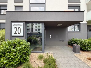 Ein modernes Gebäude mit einem Hinweisschild '20', einem Glastür und einem gepflasterten Weg mit Grünpflanzen.