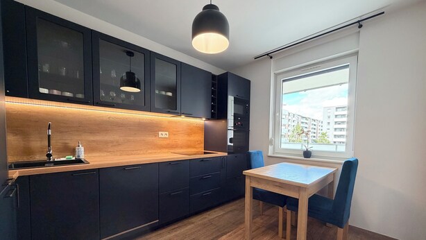 A modern kitchen with dark cabinets, a wooden countertop, and a dining area with a table and chairs. - Czartoryskiego Chic Apartment (Wrocław)