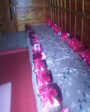 A room with a wooden wall, a bed with floral bedding, and a red carpet. - Cozzy Dira Cottage Pangalengan (Jawa Barat)