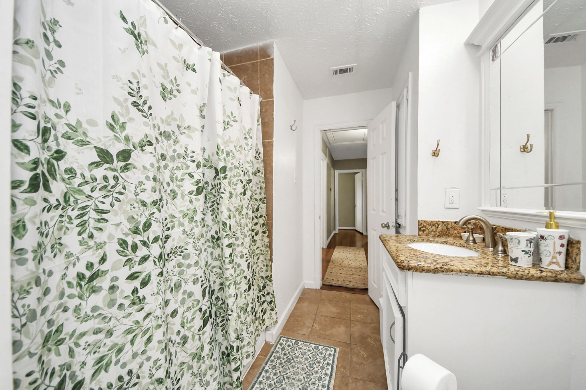 Une salle de bain avec un rideau de douche, un lavabo, un miroir et une porte donnant sur une autre pièce.