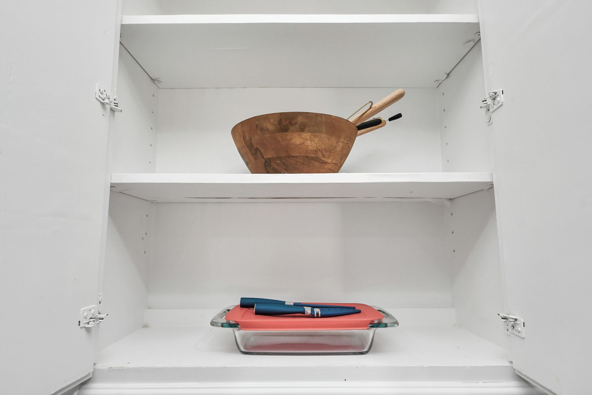 Un armario blanco con una olla de cobre en la repisa superior y un recipiente de plástico rojo con asas azules en la repisa inferior.