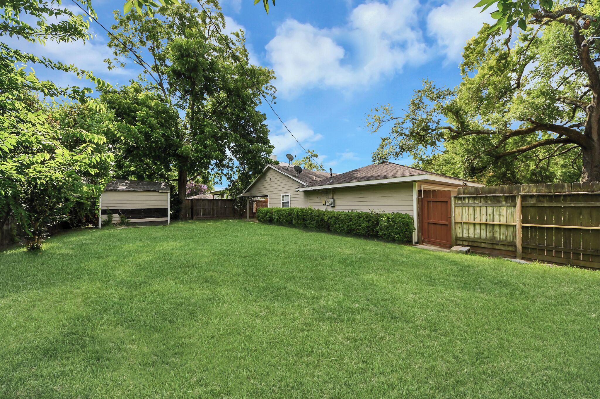 A residential backyard with a house, a garage, a wooden fence, and a large tree.