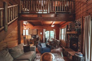 Ein Blockhaus-Interieur mit Schlafzimmer auf dem Dachboden, Kamin, Holzmöbeln und einer Wand aus Naturstein.