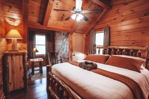 Ein Zimmer in einer Holzhütte mit einem Bett, einem Schreibtisch, einem Stuhl, einer Lampe und einem Deckenventilator.