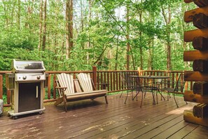 Eine Terrasse mit Grill, Stühlen und Tisch, umgeben von einem Wald.