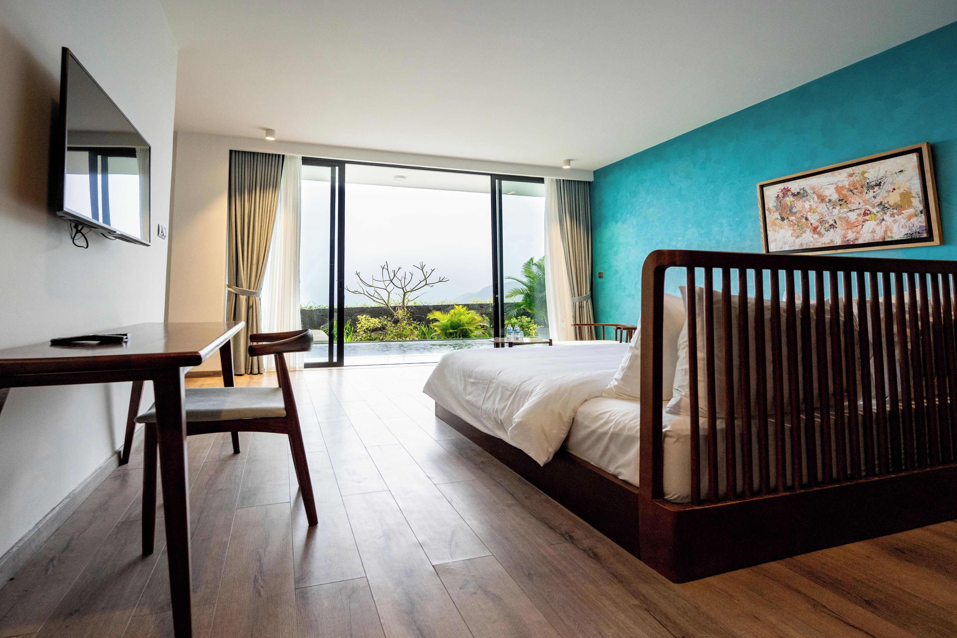 Une chambre d’hôtel avec un lit, un bureau, une chaise, une télévision et une grande fenêtre avec des rideaux.