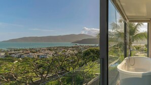 Un balcón con vistas a un pueblo costero, una bañera y abundante vegetación.
