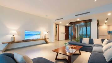 A modern living room with a flat-screen TV, a sofa, a coffee table, and a view of the outdoors.