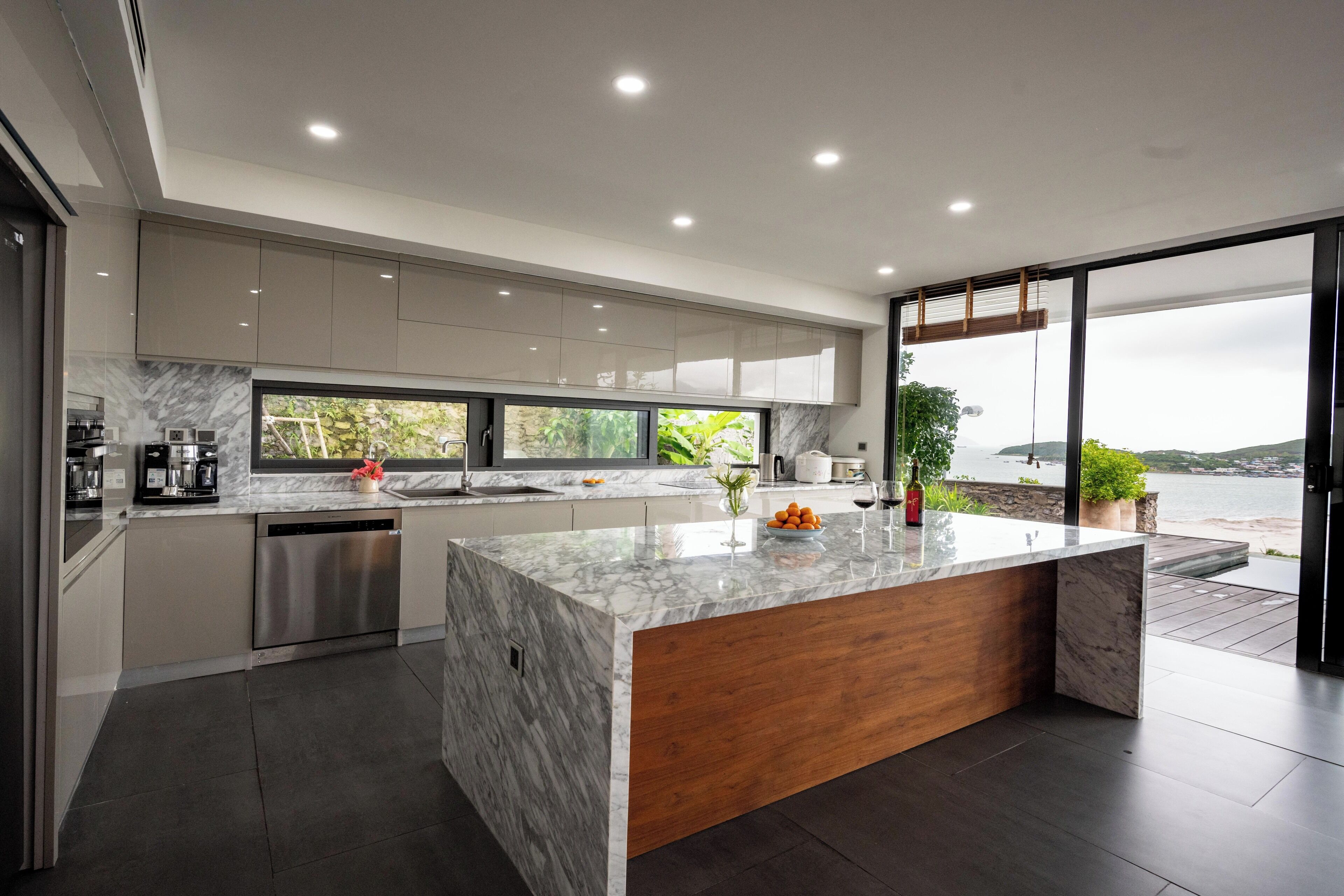 A modern kitchen with a marble island, stainless steel appliances, and a view of the sea.