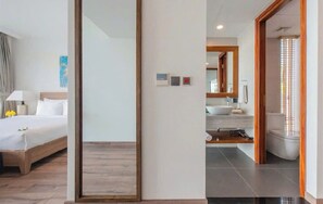 Une chambre d’hôtel avec un lit, une table de chevet, un miroir et une salle de bain équipée d’un lavabo et de toilettes.