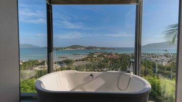 A modern bathroom with a freestanding bathtub, large windows, and a view of a coastal landscape.