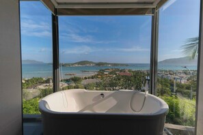 A modern bathroom with a freestanding bathtub, large windows, and a view of a coastal landscape. - Anh Nguyen Oceanfront Villas (Nam Nha Trang)
