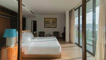 A hotel room with a large bed, a desk, a chair, a small table, a lamp, and a painting.
