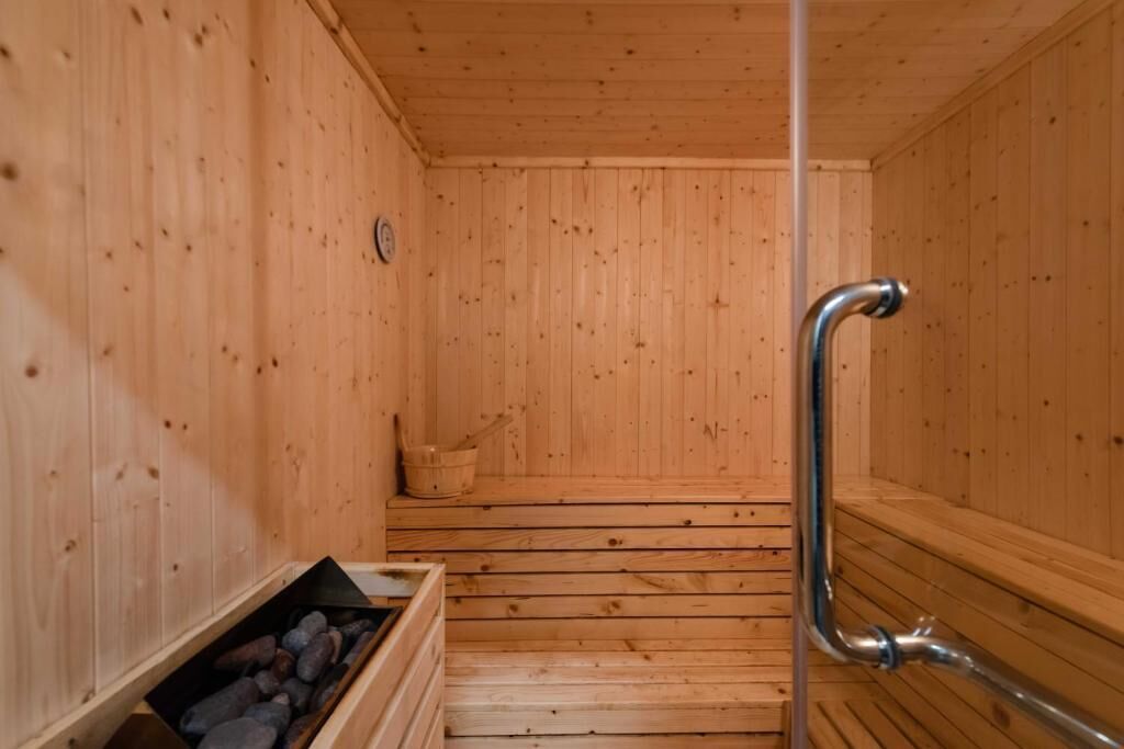 A wooden sauna with a bench, a metal handrail, and a stone-filled container.