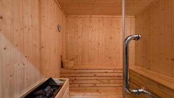 A wooden sauna with a bench, a metal handrail, and a stone-filled container.