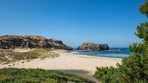 Paesaggio costiero con spiaggia sabbiosa, scogliere rocciose e cielo azzurro intenso.