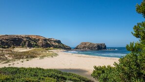 Eine Küstenlandschaft mit Sandstrand, felsigen Klippen und blauem Himmel.